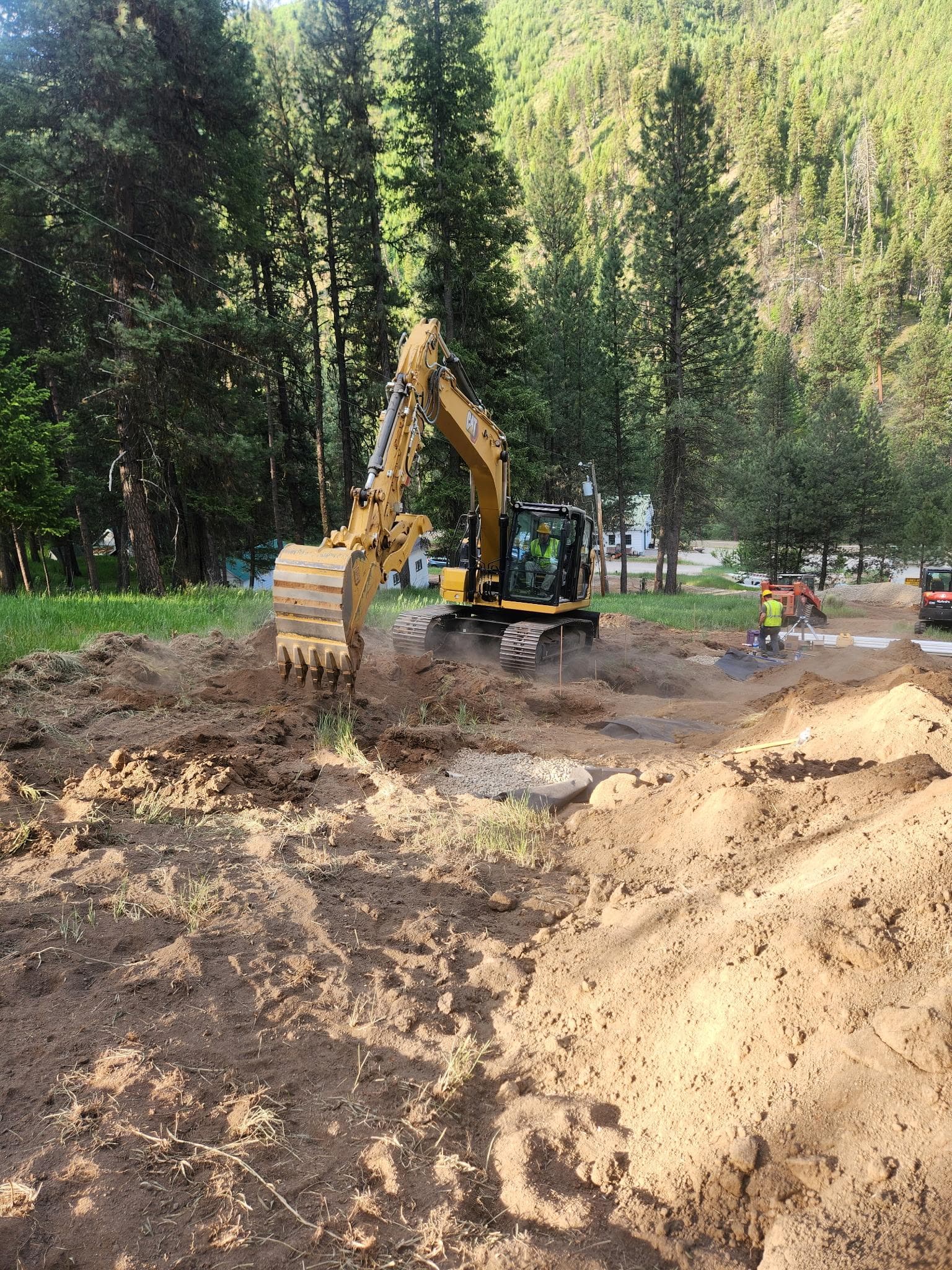 Wide excavation view showing heavy equipment working across a drainfield site.